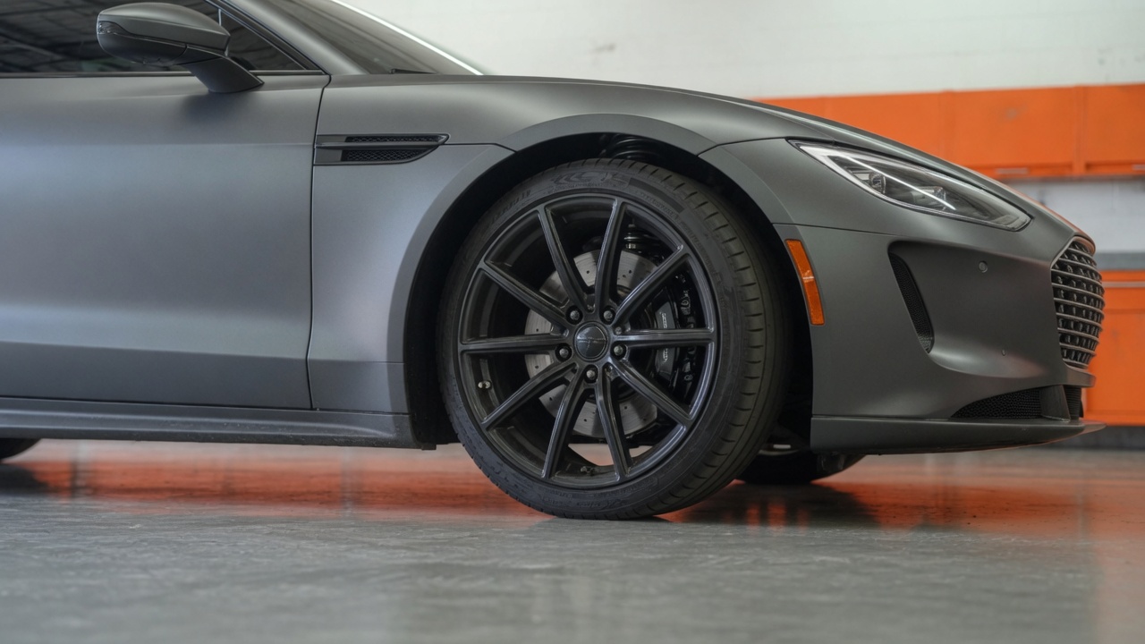 Front corner of a graphite sedan, wheel on the garage floor, rotor visible through the spokes